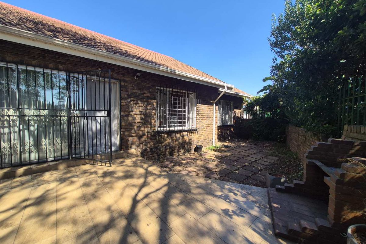 Rear exterior view of the townhouse featuring a paved patio area, built-in brick braai, and security bars on windows and doors.