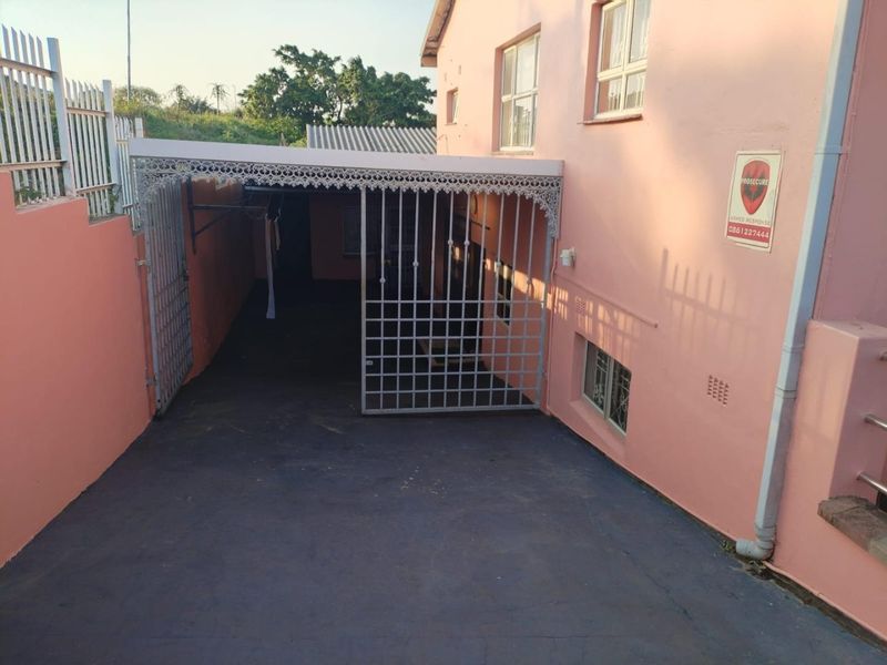 Front exterior view of the property featuring a paved driveway, covered carport area, and security gate access.