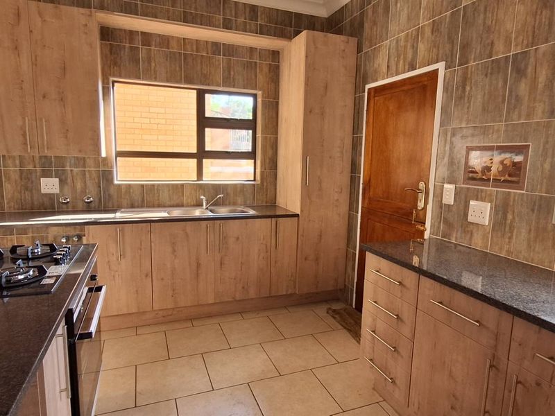 A functional kitchen featuring wood-look cabinetry, granite countertops, a gas hob, built-in oven, and tiled finishes throughout.