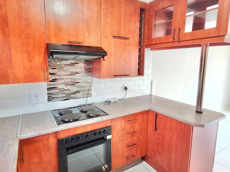 A functional kitchen featuring warm-toned wooden cabinetry, laminate countertops, a built-in oven with hob, and a classic subway tile backsplash.