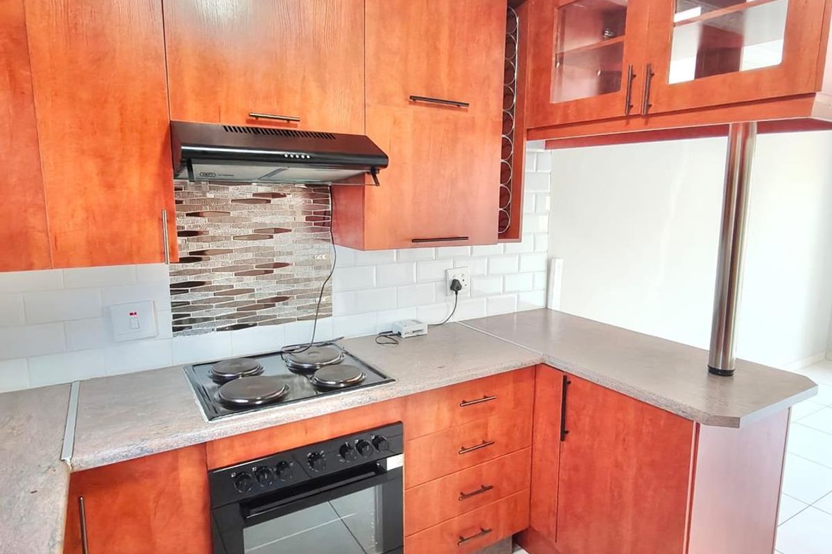 A functional kitchen featuring warm-toned wooden cabinetry, laminate countertops, a built-in oven with hob, and a classic subway tile backsplash.