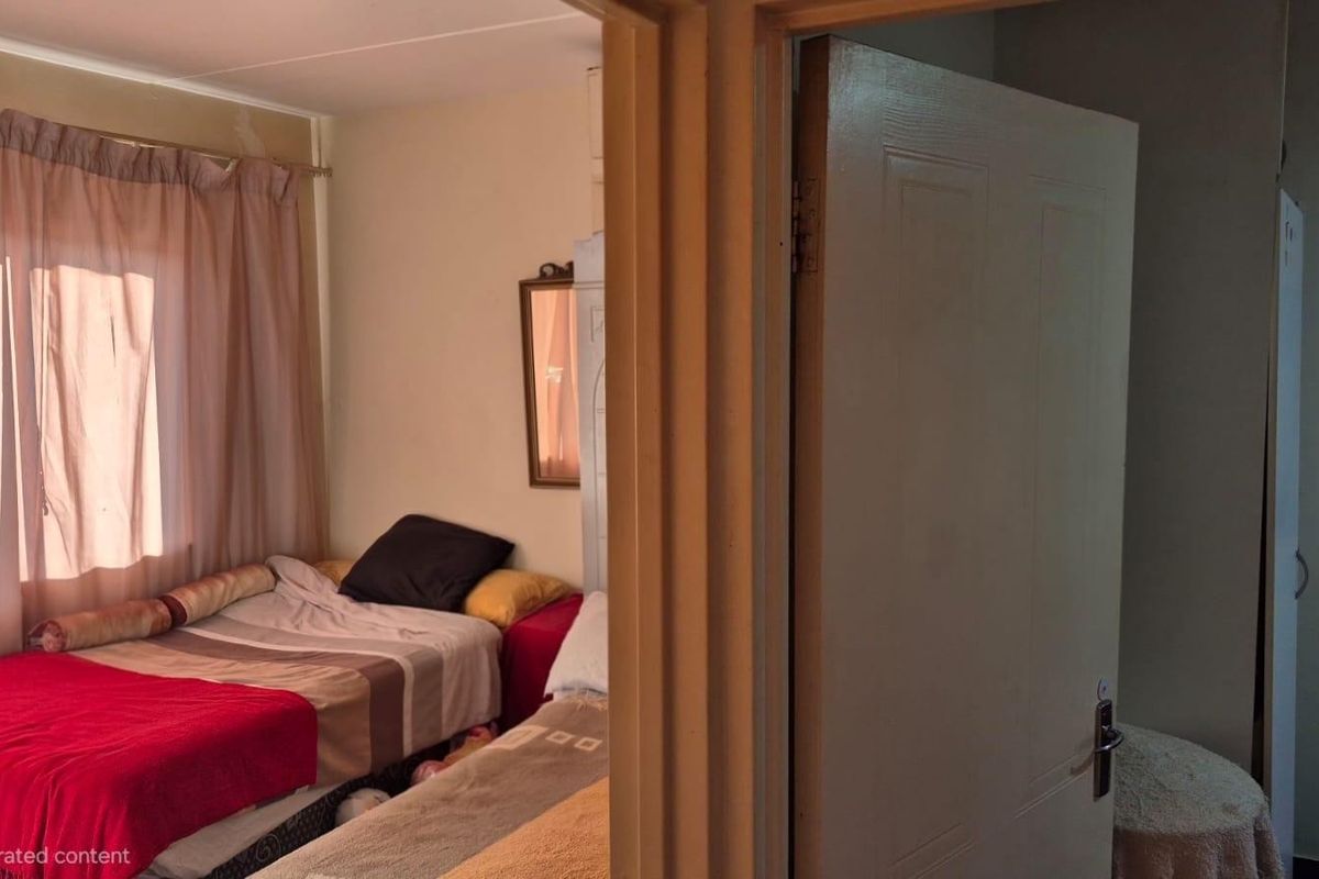 A bedroom interior featuring a window with curtains and a doorway leading into the space, showing signs of wear on the wall finishes.