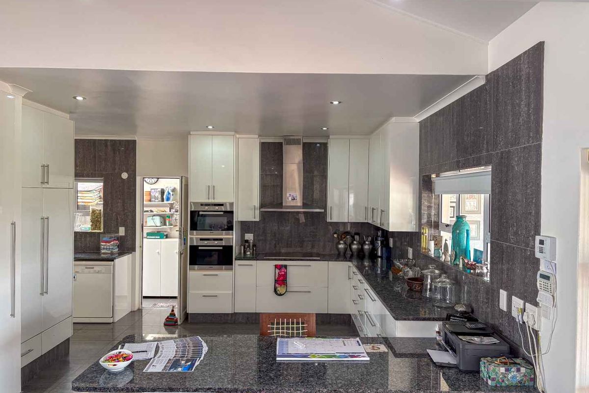 Modern kitchen featuring high-gloss cabinetry, granite countertops, built-in oven, extractor fan, and an integrated breakfast bar, with an adjacent scullery area.