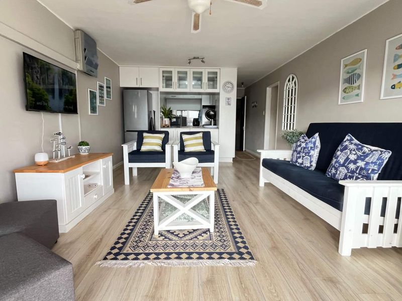 An open-plan living area featuring light laminate flooring, a ceiling fan, and a compact kitchen with built-in cabinetry.