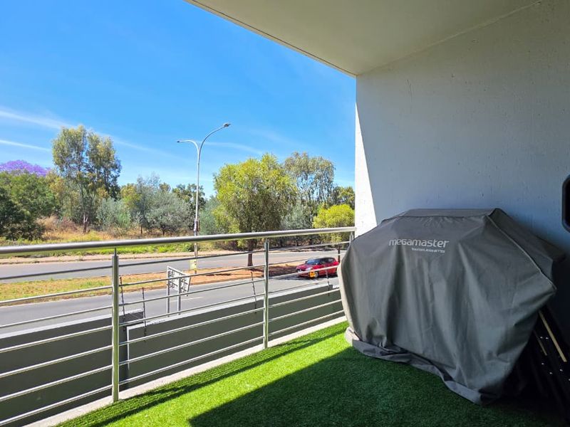 A private balcony featuring artificial grass flooring and a modern stainless steel balustrade, offering an open view of the surrounding area.