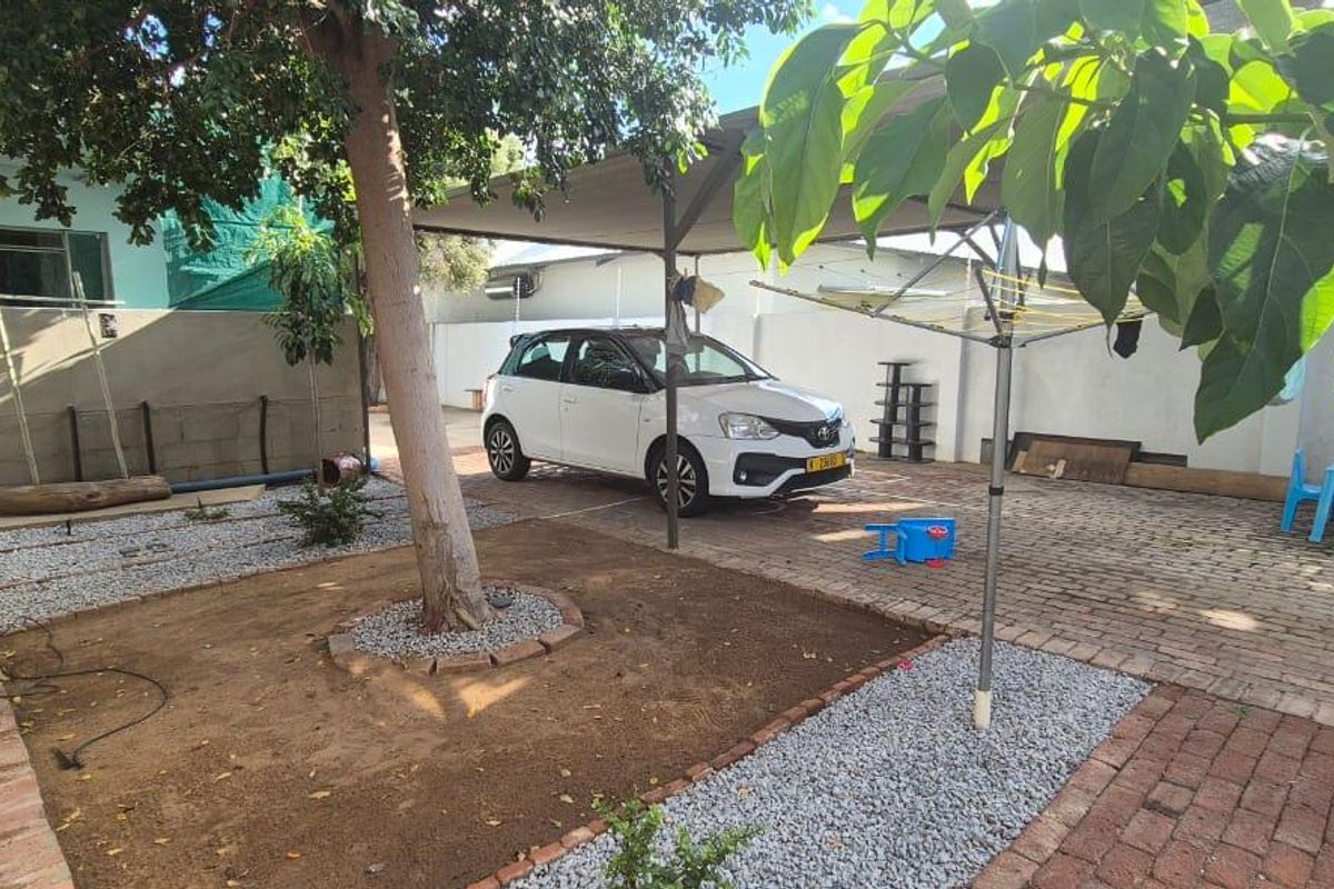 A paved rear courtyard area featuring a shaded parking space, established tree, and low-maintenance gravel landscaping.