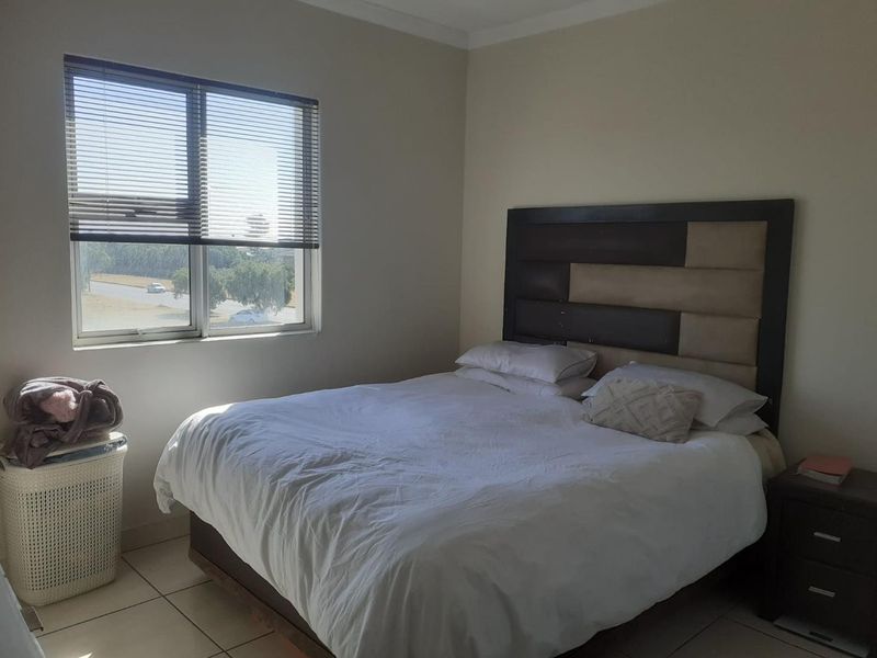 A bedroom featuring tiled flooring and a window fitted with venetian blinds, offering a functional and neutral living space.