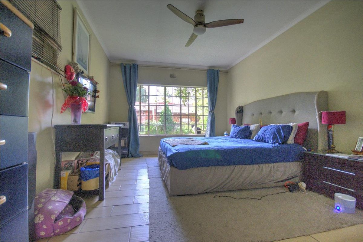 A spacious bedroom featuring tiled flooring, a ceiling fan, and a large window that provides natural light.