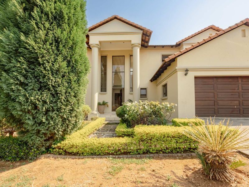 A well-maintained front elevation featuring a columned entrance, tiled roof, and a double garage with a paved driveway and landscaped garden.