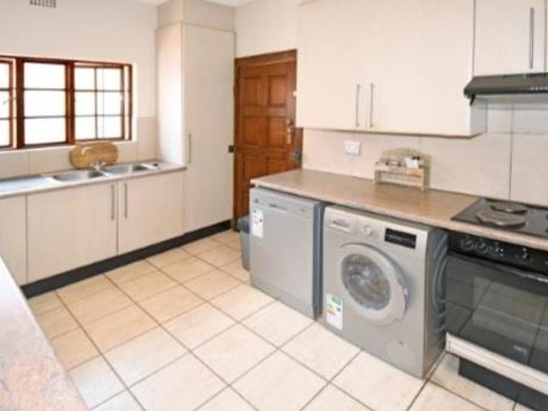 Functional kitchen featuring built-in cabinetry, electric hob, oven, extractor fan, double sink, and tiled flooring with ample counter space.