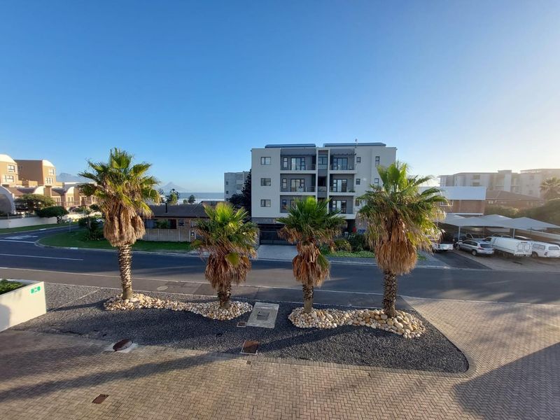 An elevated view overlooking a paved street, landscaped verge with palm trees, and surrounding residential apartment buildings.