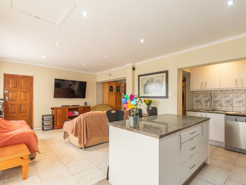 Open-plan living area featuring a functional kitchen with granite island, tiled flooring, and recessed lighting, seamlessly connecting to the lounge space.
