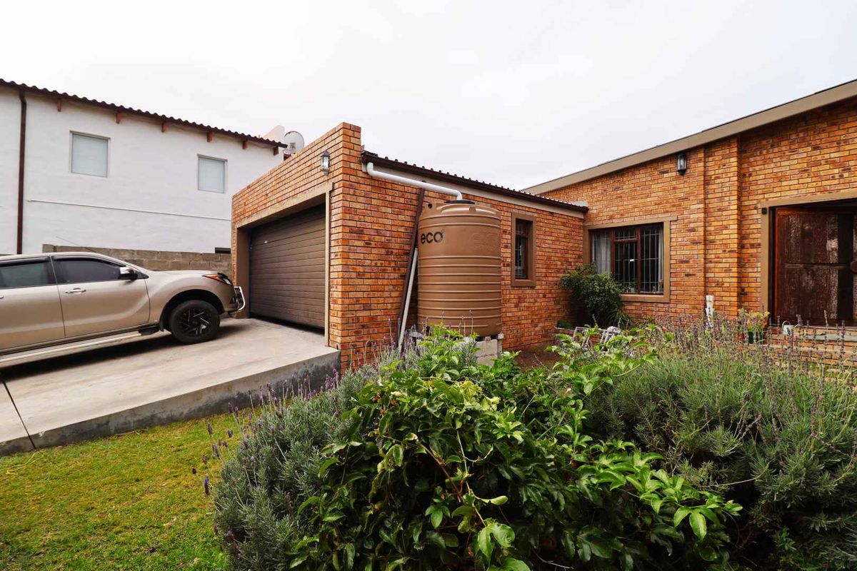 Rear exterior view featuring a face brick facade, an automated garage, and a water storage tank set within a landscaped garden area.