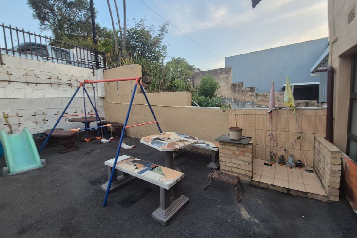 A paved rear outdoor area featuring masonry retaining walls, tiled wall accents, and a functional drainage downpipe.