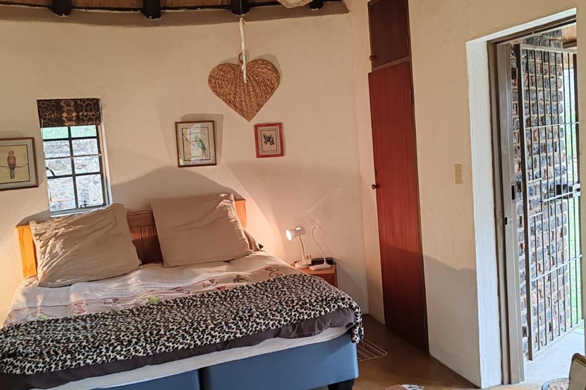 A bedroom featuring a traditional thatched roof, ceiling fan, built-in storage, and direct access to an outdoor area through a security gate.