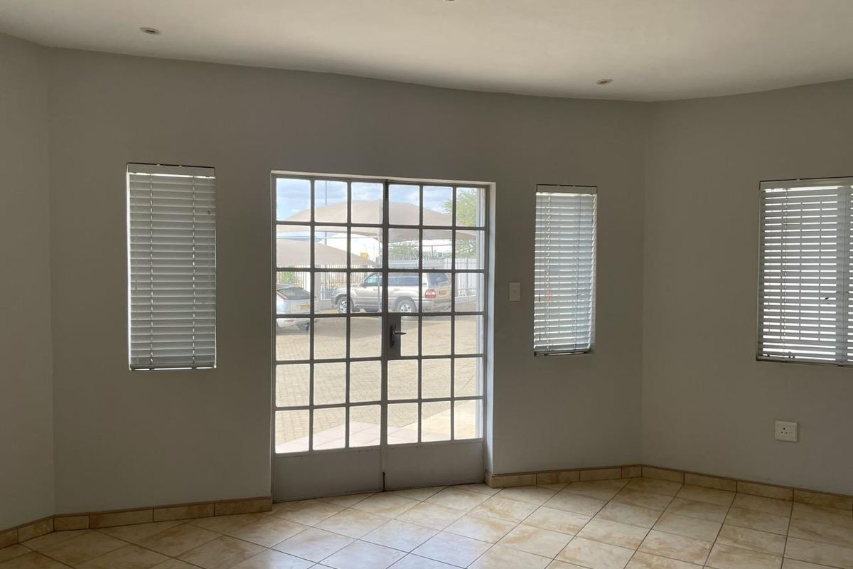 A bright, empty interior space featuring tiled flooring, recessed ceiling lighting, and a large glass-paned door providing natural light and exterior access.