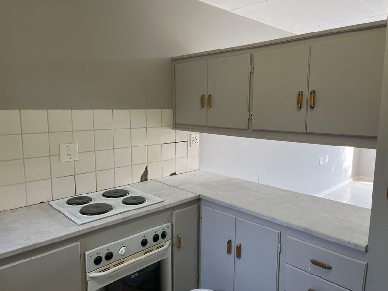 A compact kitchen featuring built-in cabinetry, an electric hob, and an oven, with visible damage to the tiled splashback area.