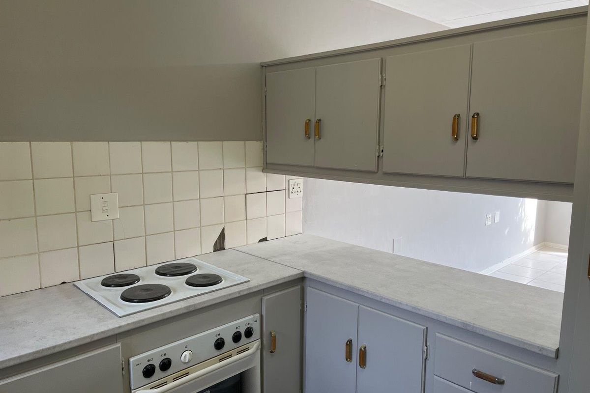 A compact kitchen featuring built-in cabinetry, an electric hob, and an oven, with visible damage to the tiled splashback area.