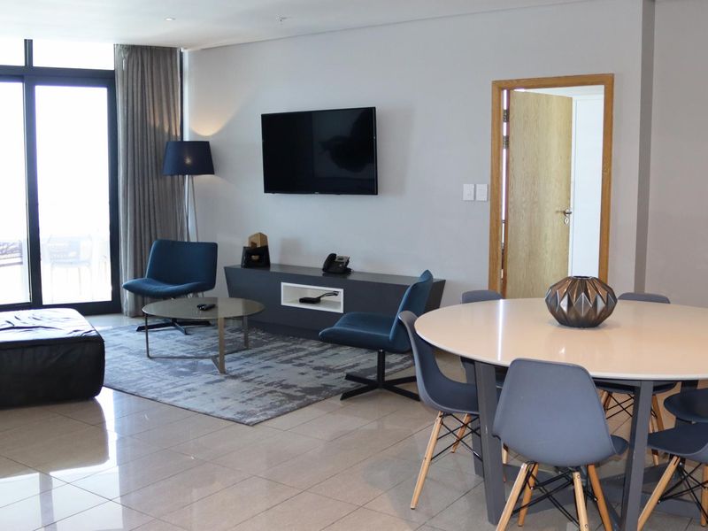 A bright open-plan living and dining area featuring tiled flooring, recessed lighting, and large sliding glass doors leading to an outdoor space.