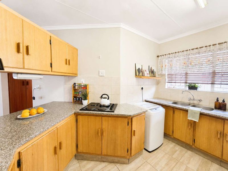 Functional kitchen featuring light wood cabinetry, granite countertops, an electric hob, and a double basin sink with tiled backsplash.