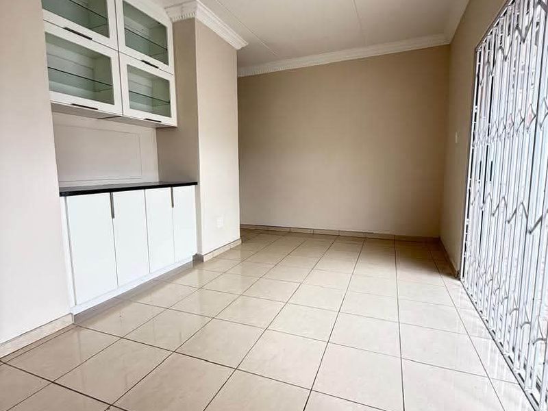 A bright, empty dining area featuring neutral tiled flooring, built-in display cabinetry, and a secure sliding door leading to the exterior.