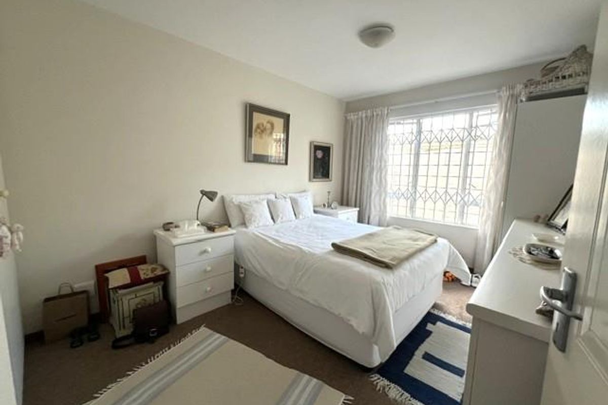 A functional bedroom featuring carpeted flooring and a window fitted with a security gate, providing natural light and basic security.