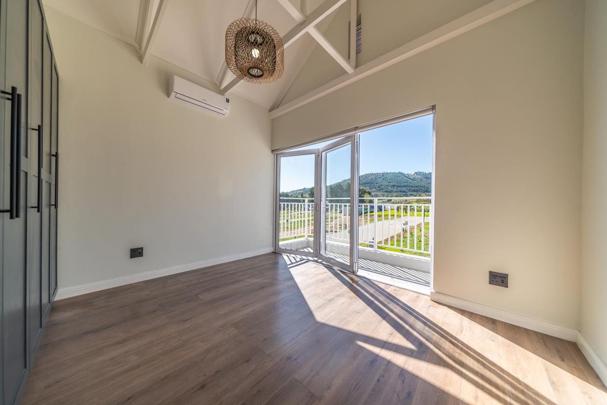 Bright bedroom featuring vaulted ceilings, built-in cabinetry, split-system air conditioning, and glass folding doors opening onto a private balcony with scenic views.