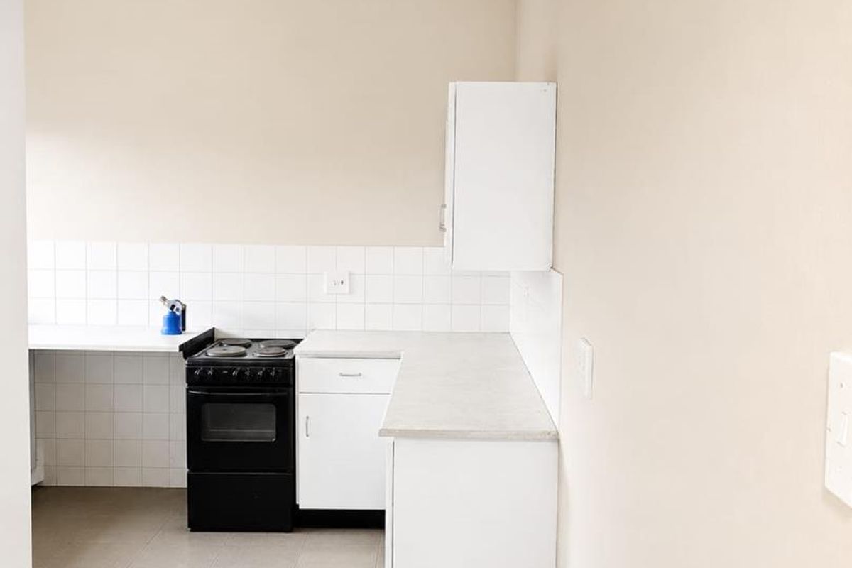 A clean, functional kitchen featuring white cabinetry, laminate countertops, a tiled backsplash, and a freestanding electric stove.