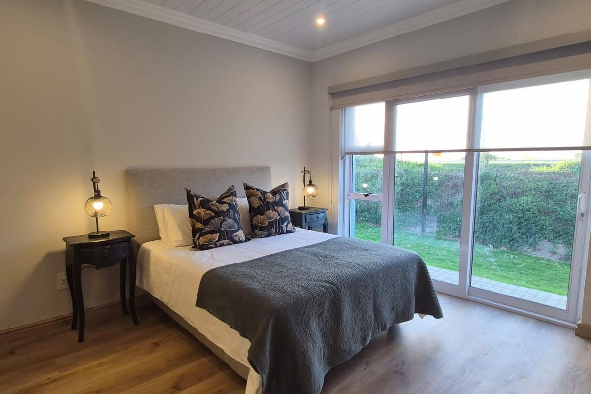 A well-maintained bedroom featuring wood-look flooring, a tongue-and-groove ceiling, and large sliding glass doors providing direct access to the garden.