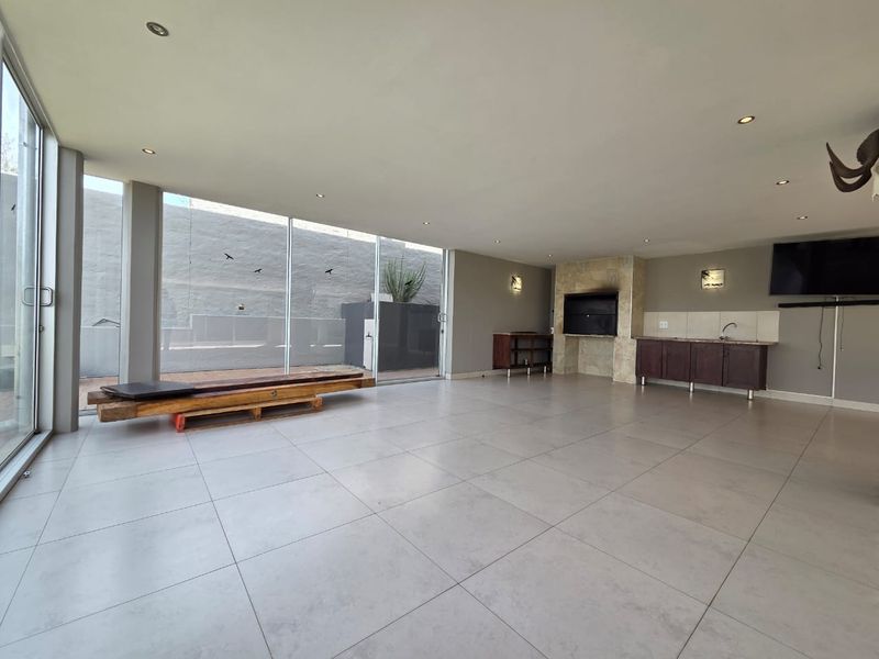 Spacious open-plan living area featuring large sliding glass doors, tiled flooring, a built-in fireplace, and a functional kitchenette area with sink and cabinetry.