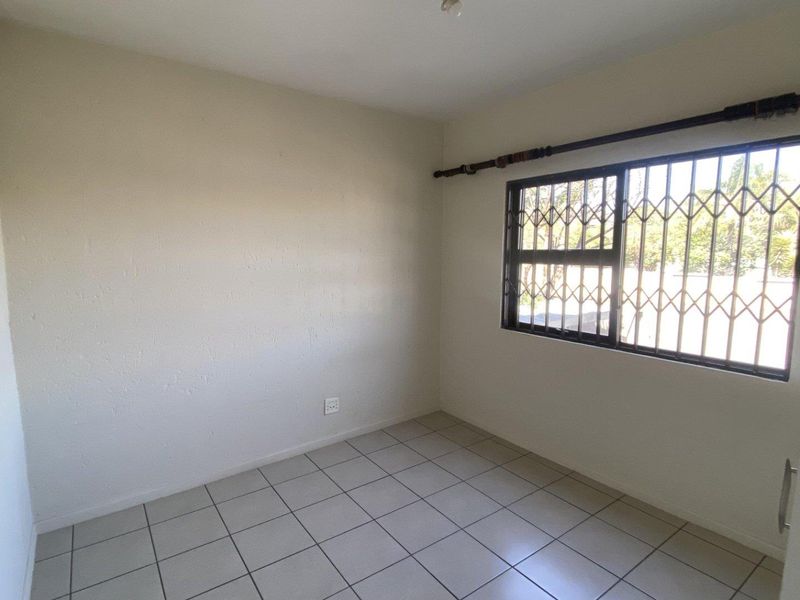 A vacant bedroom featuring neutral tiled flooring and a window fitted with security bars.