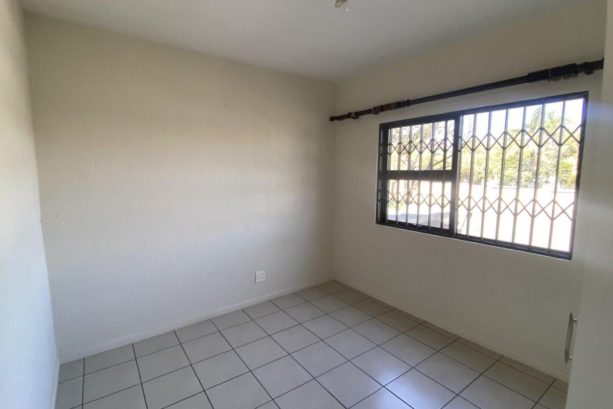 A vacant bedroom featuring neutral tiled flooring and a window fitted with security bars.