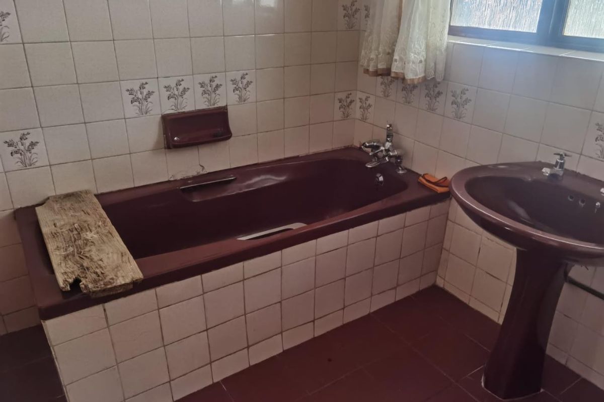 A dated bathroom featuring a dark-toned built-in bathtub and matching pedestal basin, finished with patterned ceramic wall tiles and floor tiling.