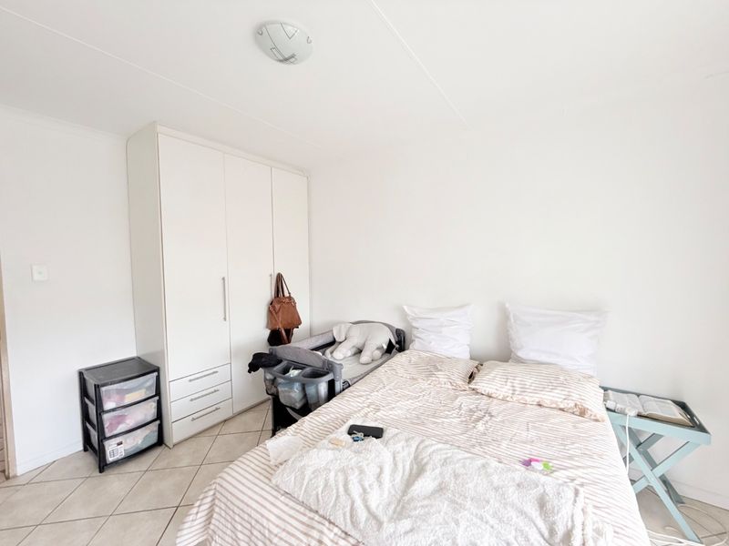 A functional bedroom featuring neutral tiled flooring and a built-in white wardrobe, offering a clean and simple space ready for personalization.