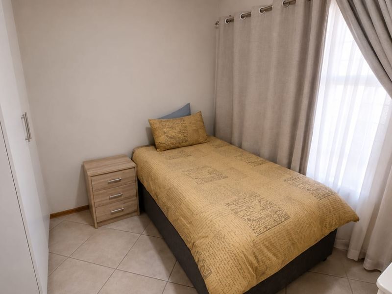 A compact bedroom featuring neutral tiled flooring, a built-in wardrobe, and window treatments, offering a clean and functional living space.
