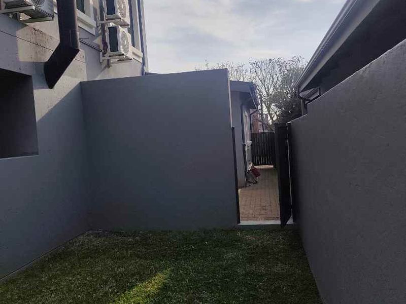 A side yard area featuring a small lawn, paved pathway, and exterior wall-mounted air conditioning units.