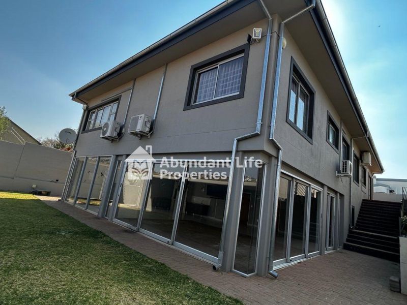 Rear view of a modern two-story house featuring extensive sliding glass doors, paved patio area, and an external staircase leading to the upper level.