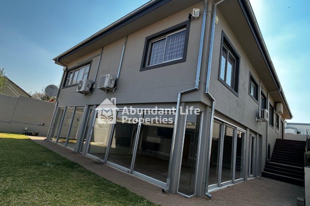 Rear view of a modern two-story house featuring extensive sliding glass doors, paved patio area, and an external staircase leading to the upper level.