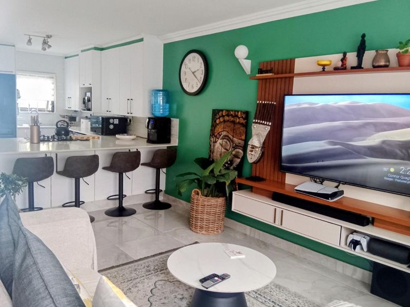 Open-plan living area featuring a modern kitchen with stone countertops and a gas hob, seamlessly connected to a lounge with a built-in media unit.