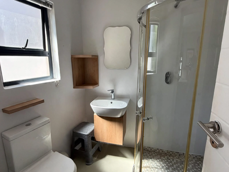 A compact, modern bathroom featuring a curved glass shower enclosure, wall-mounted vanity with basin, and a clean, neutral aesthetic.