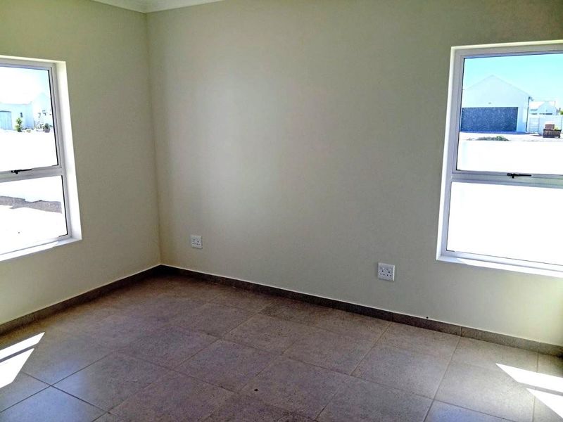 A bright, empty bedroom featuring neutral tiled flooring and dual windows, providing a clean and versatile space ready for personalization.