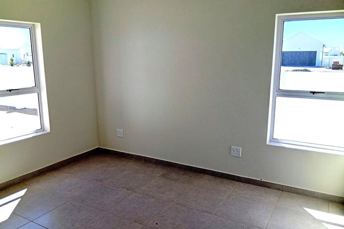 A bright, empty bedroom featuring neutral tiled flooring and dual windows, providing a clean and versatile space ready for personalization.