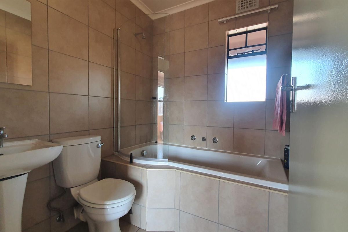 A functional bathroom featuring a pedestal basin, toilet, and a built-in bathtub with a glass shower screen and tiled wall finishes.