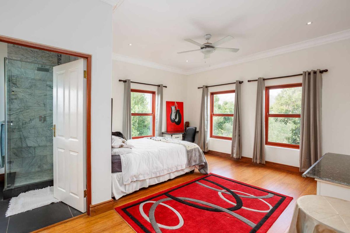 Spacious bedroom featuring warm wooden flooring, large windows with natural light, and an en-suite bathroom with a glass-enclosed shower.