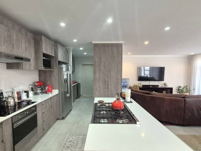 Modern open-plan kitchen featuring wood-grain cabinetry, stone countertops, a central island with a gas hob, and integrated appliances, flowing into the living area.