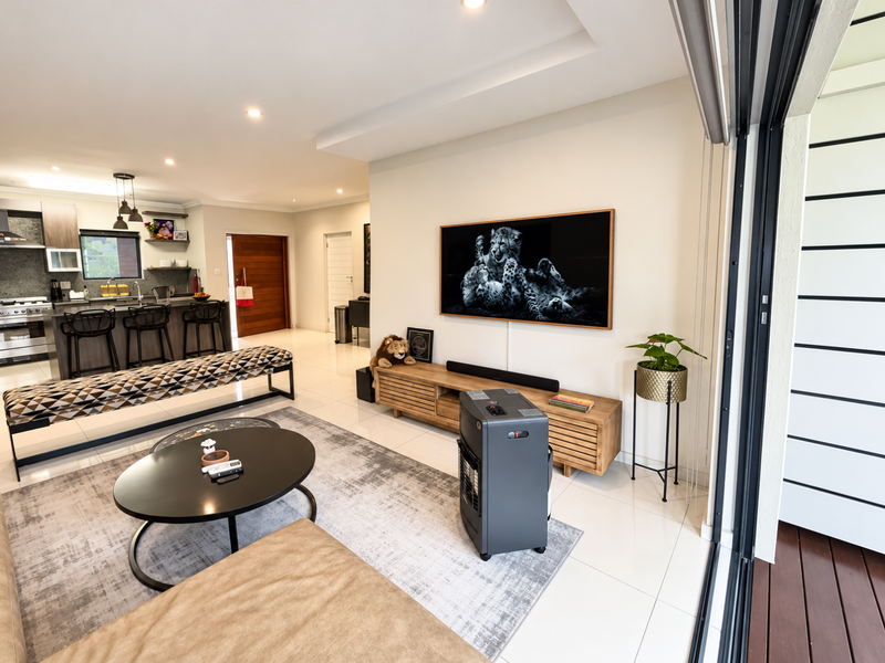 Modern open-plan living area featuring tiled floors, recessed lighting, and a seamless transition to an outdoor patio through large sliding glass doors.