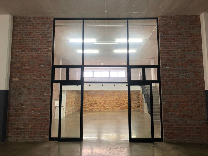 Spacious open-plan industrial style unit featuring exposed brick walls, polished concrete floors, and a large black metal framed glass partition with mezzanine access.