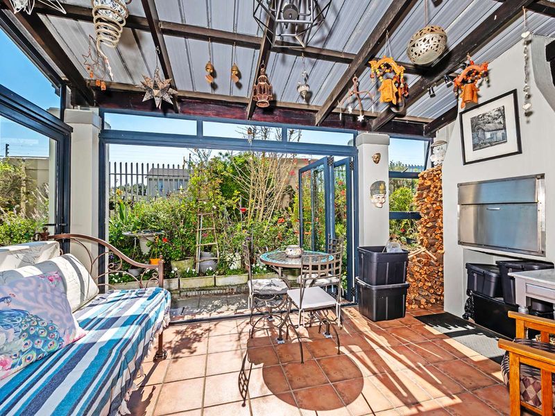 A covered patio featuring a built-in braai, tiled flooring, and folding glass doors that open onto a lush garden area.
