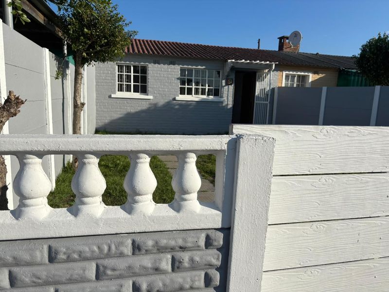 Front view of a single-story brick house featuring a precast concrete boundary wall, security gate, and tiled roof.