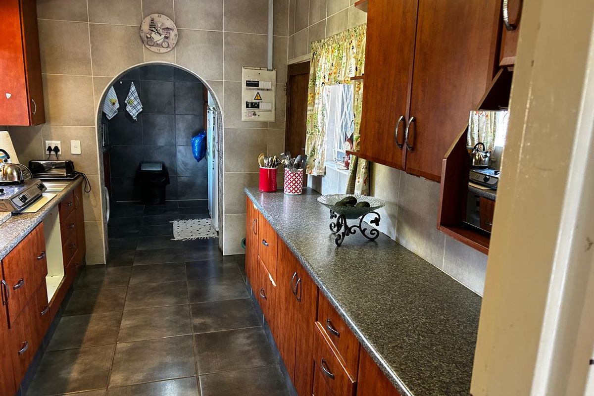 A functional kitchen featuring wood-veneer cabinetry, stone-look countertops, and tiled flooring, with an arched doorway leading to an adjacent utility area.